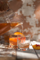 Ice tea with nectarine, peach. In a jug. A woman's hand pours into a glass. A refreshing summer drink.