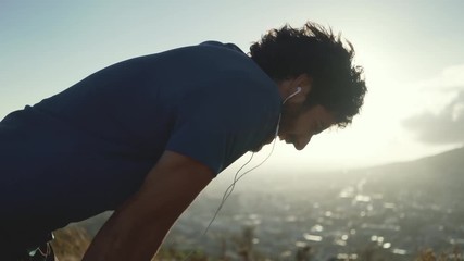 Tired male athlete with earphones in his ears relaxing after exercising