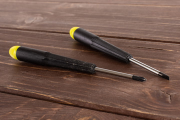 Group of two whole screwdrivers with a yellow black plastic handle work item on brown wood