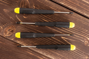 Group of four whole screwdrivers with a yellow black plastic handle work item flatlay on brown wood