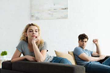 selective focus of upset blonde woman sitting on sofa near man after quarrel