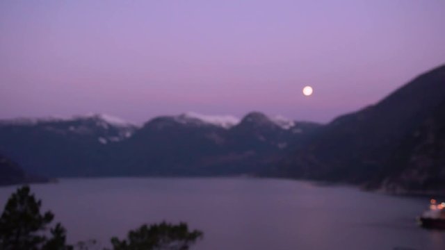 super wolf blood moon still up while sun rising creating purple moon, camera  pans down puts moon and mountains into focus