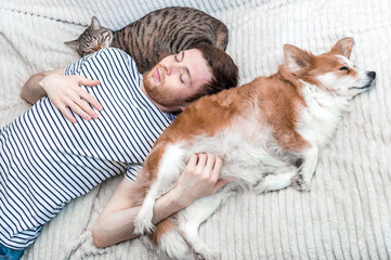 Portrait of a young sleeping man with his dog and cat on the bed