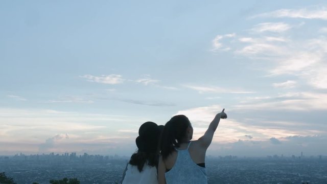 Two Teenage Girls Taking A Photo And Pointing At The Sky Of The City On A Rooftop