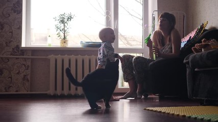 a young beautiful woman blowing soap bubbles inside the room with big window on background and a little baby boy and a black cat are catching this bubbles in slow motion 4K video - Powered by Adobe