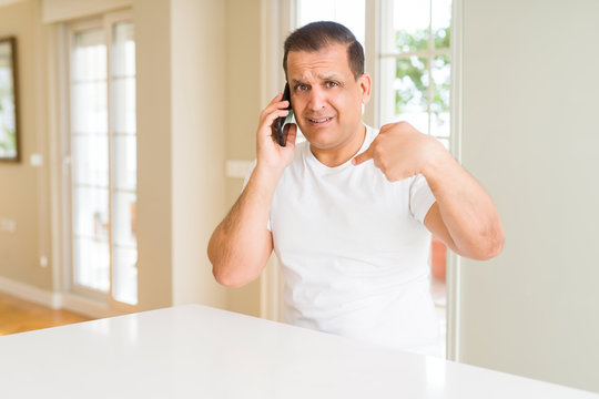 Middle age man calling using smartphone with surprise face pointing finger to himself