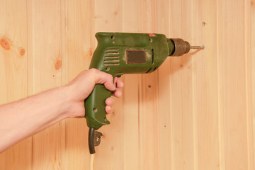 man's hand holds an old electric drill and drills a wooden wall of clapboard