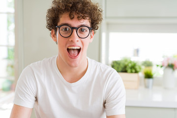 Young handsome man wearing glasses celebrating crazy and amazed for success with arms raised and open eyes screaming excited. Winner concept