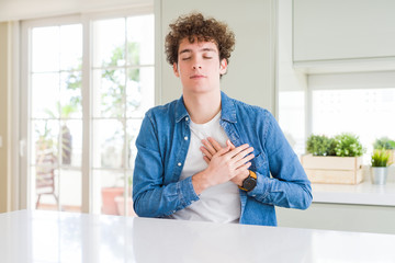 Naklejka na ściany i meble Young handsome man wearing casual denim jacket at home smiling with hands on chest with closed eyes and grateful gesture on face. Health concept.