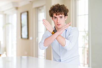 Young business man with curly read head Rejection expression crossing arms doing negative sign,...