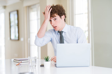Naklejka premium Young business man working with computer laptop at the office surprised with hand on head for mistake, remember error. Forgot, bad memory concept.
