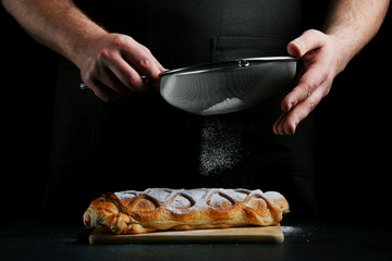 man powder of sugar to pie on dark background. decorating dessert concept with ingredients
