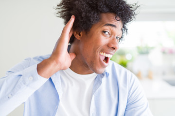 Handsome african american man with afro hair smiling with hand over ear listening an hearing to rumor or gossip. Deafness concept.