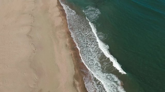Small waves hitting the shore - aerial panning from blue sky to the water