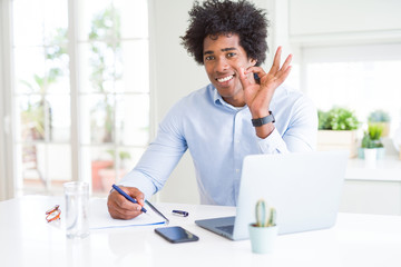 African American business man working writing on notebook doing ok sign with fingers, excellent symbol