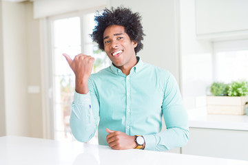 African American business man wearing elegant shirt smiling with happy face looking and pointing to the side with thumb up.