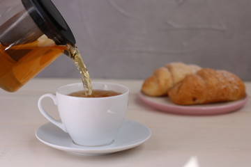 tea pouring into cup and croissant dessert on light wooden background