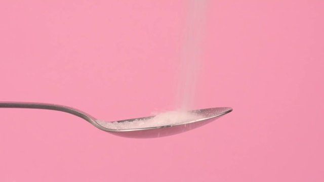 Conceptual image of white sugar falling on spoon with pastel background.