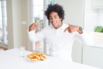 Fototapeta na wymiar African American hungry man eating hamburger for lunch looking confident with smile on face, pointing oneself with fingers proud and happy.