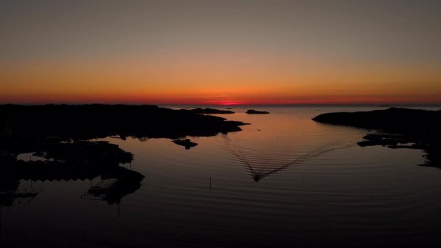 Drone flying smoothly with small boat in foreground and sunset background