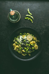 Green potatoes salad with roasted green asparagus, edamame soybeans, lime and green peas on dark rustic kitchen table background, top view. Copy space. Healthy vegetarian food .