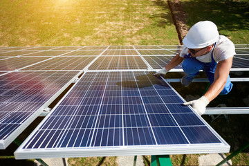 Innovative solar panels installing by young worker wearing blue uniform and protective helmet....