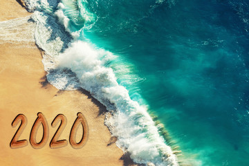 Year 2020 new year greeting text on a beach with turquoise water