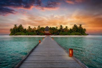 Holzsteg führt zu einer tropischen Paradiesinsel mit Palmen und Sandstrand bei Sonnenuntergang, Malediven, Indischer Ozean - obrazy, fototapety, plakaty