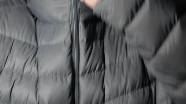 Middle aged white male puts on grey puffer jacket and does up the zipper. LOCKED DOWN SHOT. CLOSE UP