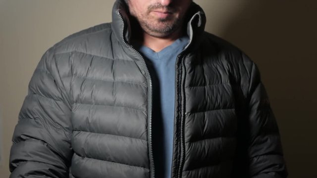 Middle aged white male unzips puffer jacket and then does up the zipper. LOCKED DOWN SHOT.
