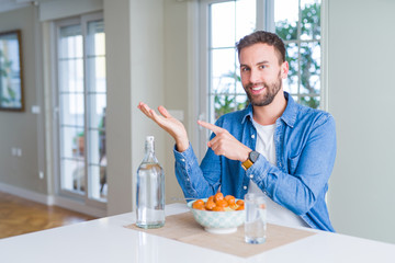 Handsome man eating pasta with meatballs and tomato sauce at home amazed and smiling to the camera while presenting with hand and pointing with finger.