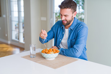 Handsome man eating pasta with meatballs and tomato sauce at home while smiling at the camera