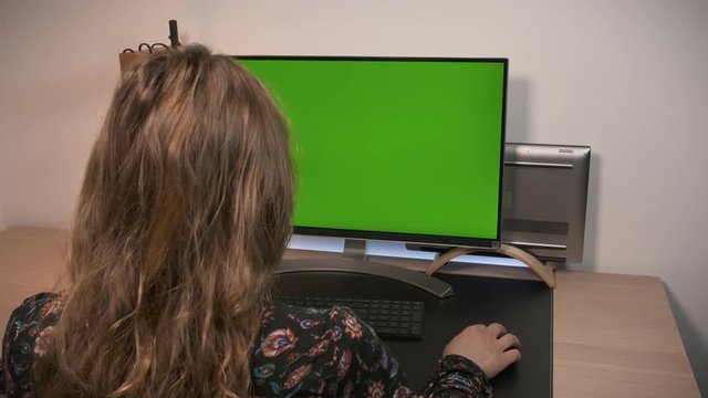 Woman working in a modern personal computer, with Mock-up Green Screen Display Standing on the Desk of the Office.