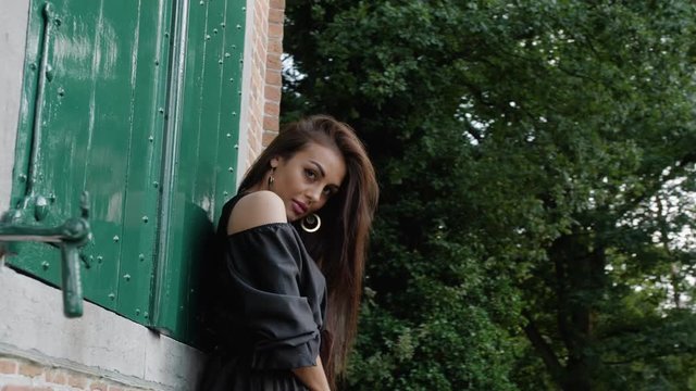 Russian girl wearing a black dress is sensually looking to the camera, while it's panning behind a brick wall.