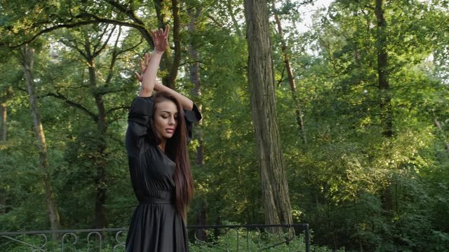 East European girl is enjoying herself dancing in a black dress in an isolated park.