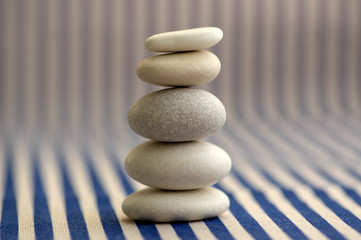 Fototapeta na wymiar Harmony and balance, pebble rock cairn, simple poise stones on white and blue striped background, rock zen sculpture, one tower