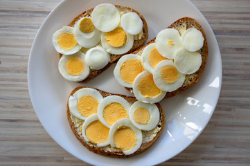 Sliced hard boiled eggs on common czech bread with butter on white plate on light wooden table
