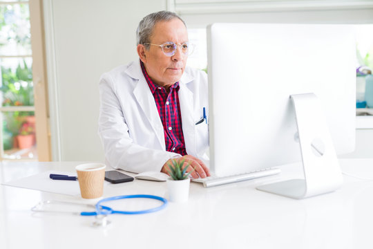 Senior doctor man at the clinic concentrated working with computer looking for a cure