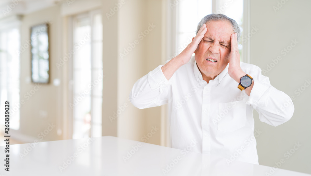 Sticker Handsome senior man at home with hand on head for pain in head because stress. Suffering migraine.