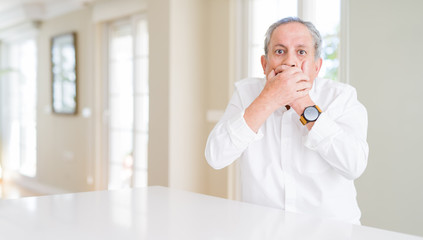 Fototapeta premium Handsome senior man at home shocked covering mouth with hands for mistake. Secret concept.