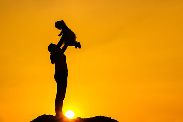 The family silhouette of the mother and child standing watch the sunset and the sky in orange in evening