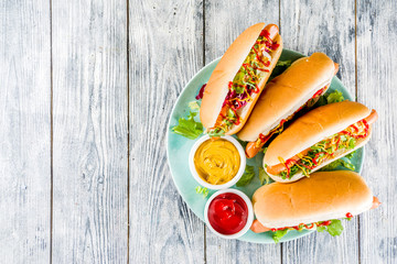 Homemade hot dogs with fresh greens, sausages and sauces, white wooden background copy space top...