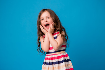 baby girl brunette in colorful dress smiling, isolate on blue background, children's emotions,Close-up portrait of dark-haired little girl  smiling on isolated background 