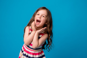 baby girl brunette in colorful dress smiling, isolate on blue background, children's emotions,Close-up portrait of dark-haired little girl  smiling on isolated background 