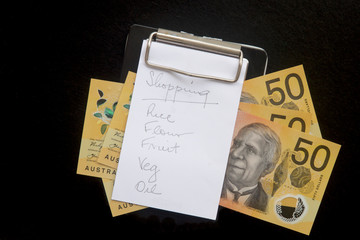 Shopping list on a clipboard with Australian fifty dollar notes.