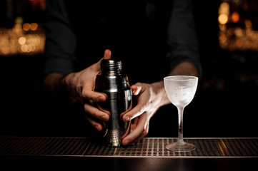Bartender holds shaker with alcohol cocktail glass nearby