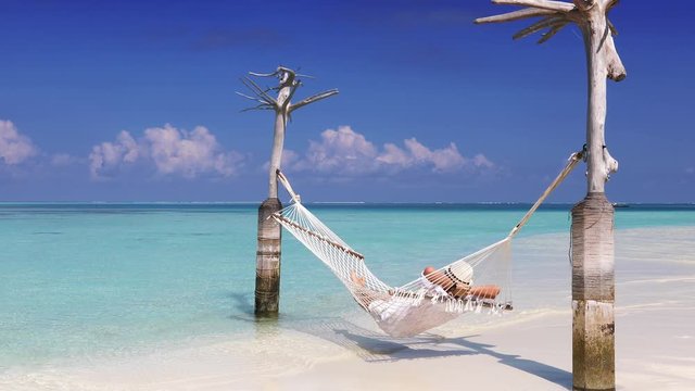Man in white summer clothes relaxes in a hammock over turquoise, tropical waters