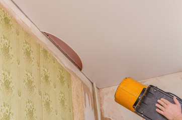 Working with a hot water bottle performs installation of a stretch ceiling. The installer performs the work on the repair of the ceiling