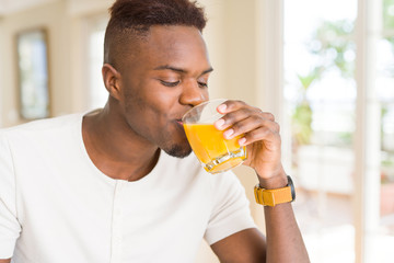 Fototapeta premium Handsome young african man drinking a glass of fresh natural orange juice enjoying fruit refreshment