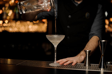 Bartender makes an alcohol cocktail with sieve on a jar